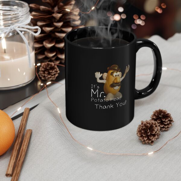 It's Mr. Potato Head Thank You black ceramic mug, full of coffee next to a scented candle